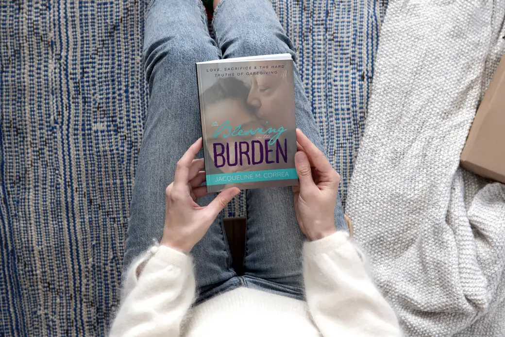 A woman reading The Blessing in the Burden
        on a couch, the book held in her lap